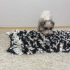 A small dog sniffing a black and white snuffle mat designed for mental stimulation.